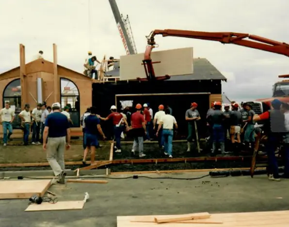 Group of construction workers wearing helmets building a wooden house frame with a crane lifting a panel.