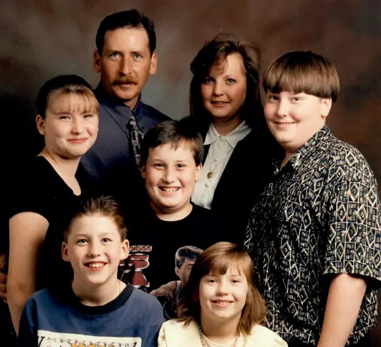 Group portrait of two adults and five children smiling against a brown studio backdrop.