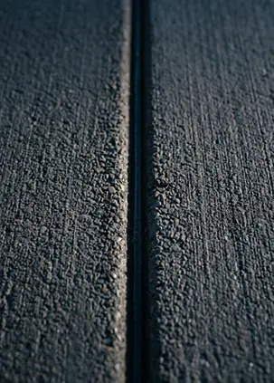 Close-up of a narrow joint between two textured dark concrete slabs.