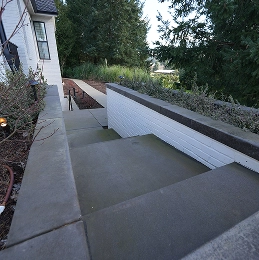 Concrete outdoor stairs descending beside a white building with greenery around.