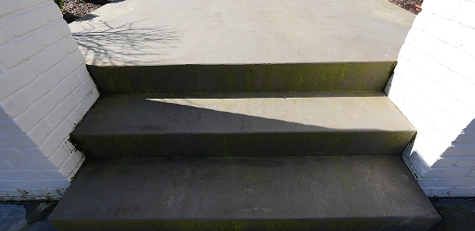 Concrete steps with moss and shadows between white brick walls on each side.
