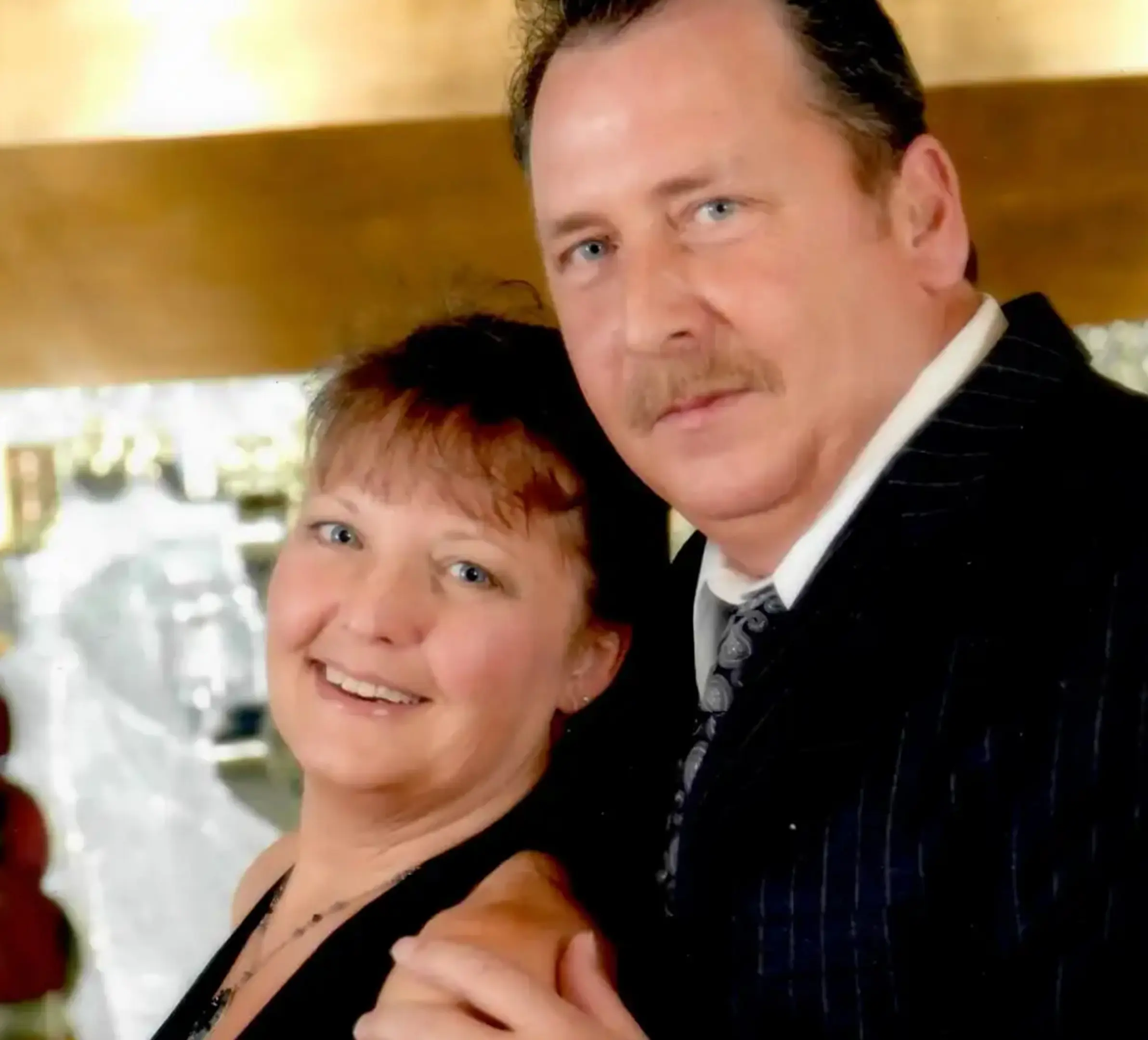 Middle-aged couple posing closely together, the woman smiling and the man in a suit with a tie.