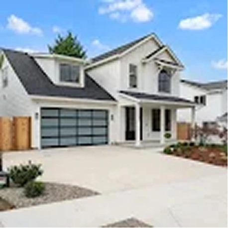 Modern two-story white house with a black roof and a driveway under a blue sky.