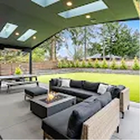 Covered patio with sectional sofa, fire pit table, picnic table, and skylights overlooking a green yard.