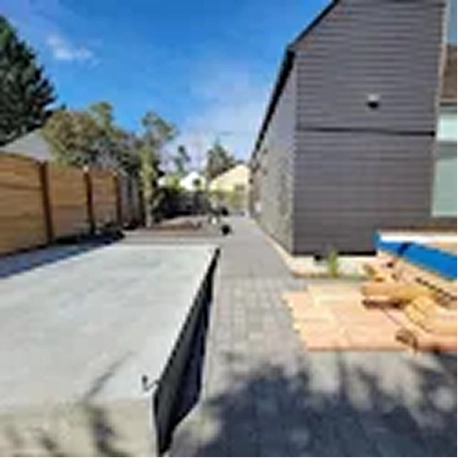 Outdoor backyard with a concrete pool under construction beside a grey house and wooden fence.