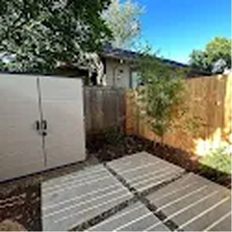 Small backyard with white shed, wooden fence, and spaced white stepping stones on ground.