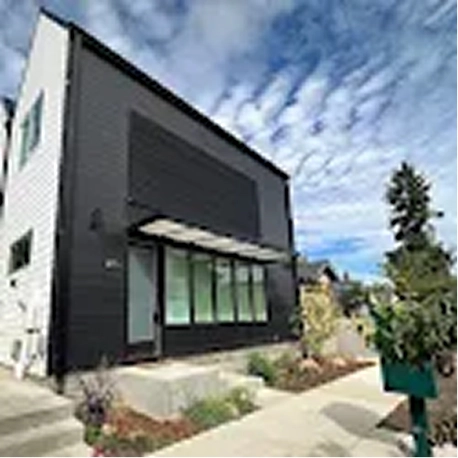 Modern black and white building with large windows and a partly cloudy sky above.