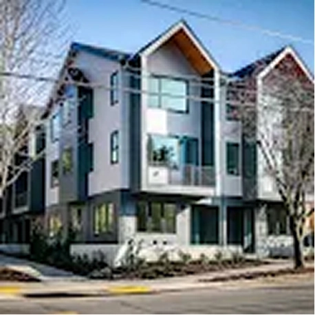 Modern three-story residential building with large windows and peaked roof sections on a street corner.