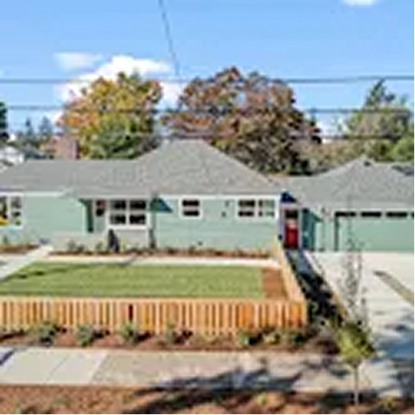 Single-story green house with a fenced front yard and driveway under a partly cloudy sky.