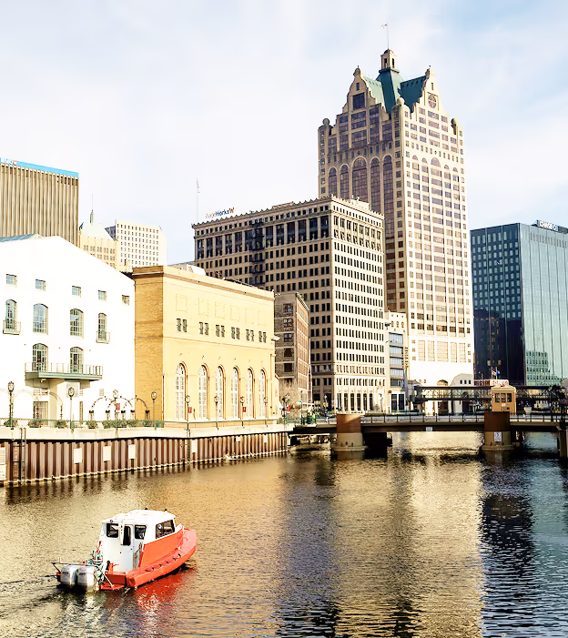 Red and white boat on a river in front of downtown Milwaukee buildings on a sunny day.