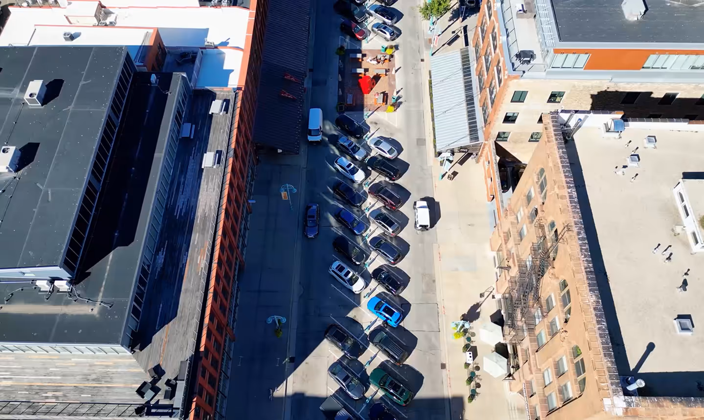 Aerial view of parked cars between urban buildings casting shadows on a sunny day.