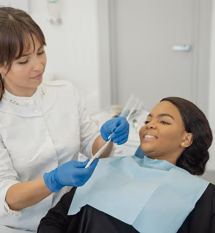 Dentist wearing blue gloves showing dental tool to a smiling patient in a dental chair.