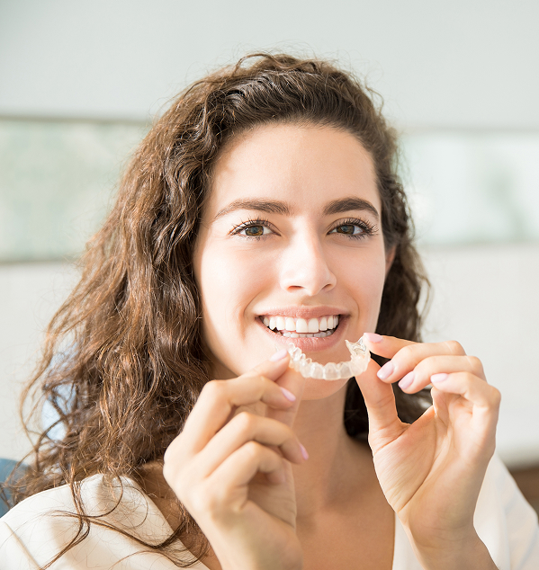 Smiling woman holding a clear dental aligner in both hands.