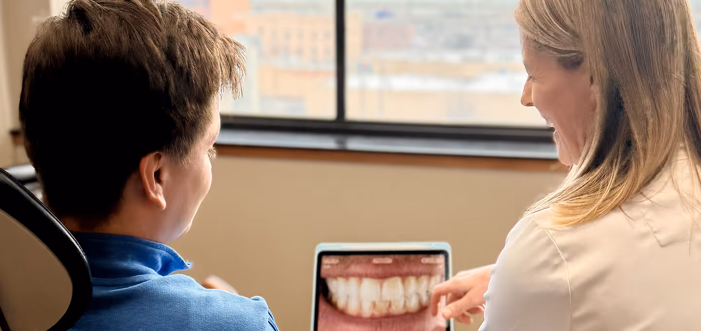 Dentist showing dental X-ray image of teeth to a male patient on a tablet.