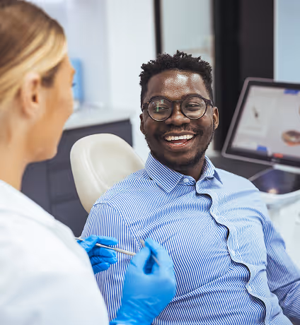 Smiling man wearing glasses sitting in dental chair talking to dentist in gloves.