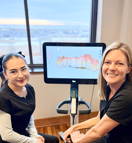 Two dental professionals smiling in front of a screen displaying a 3D digital model of teeth.