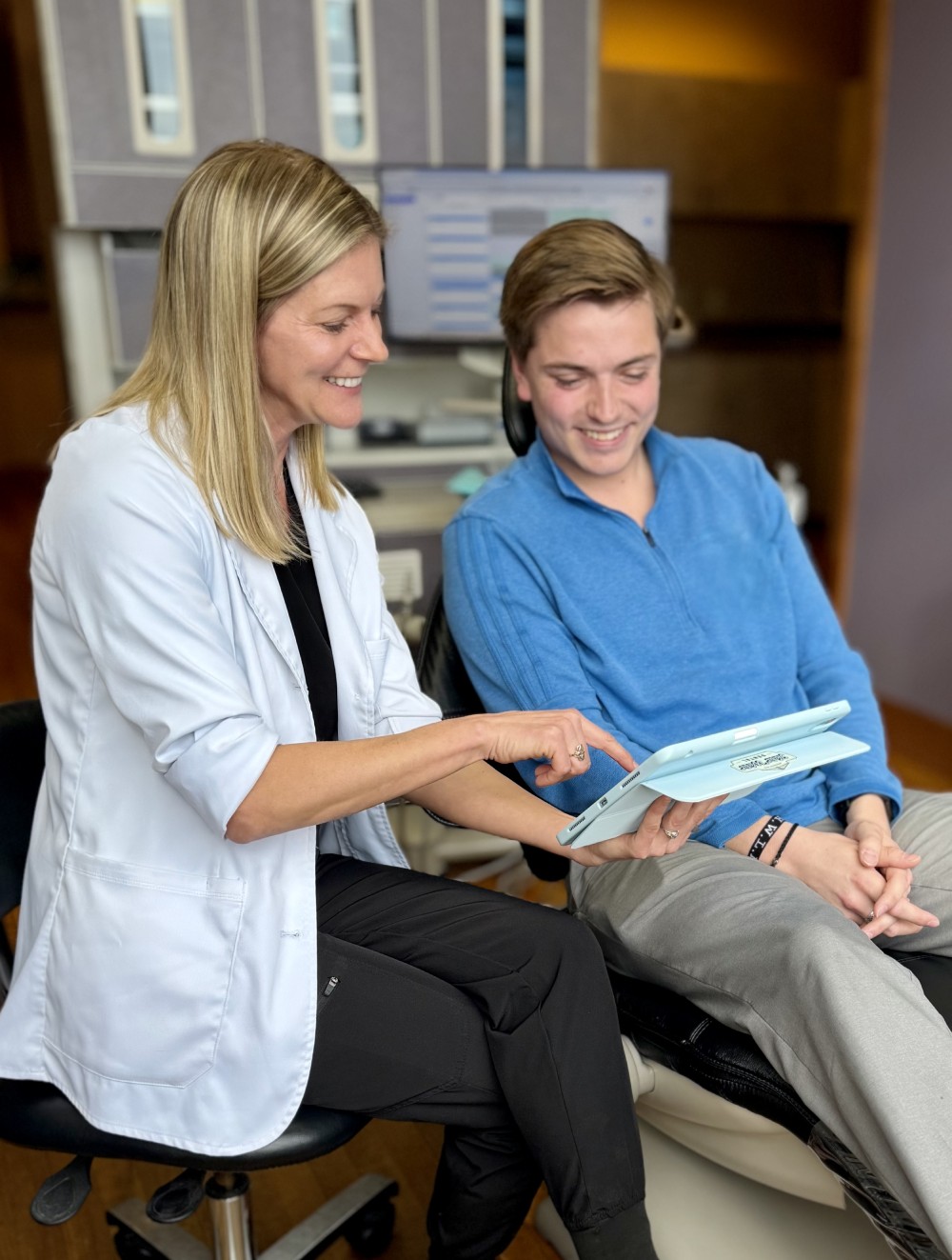 Female healthcare professional showing something on a tablet to a smiling young male patient seated beside her.