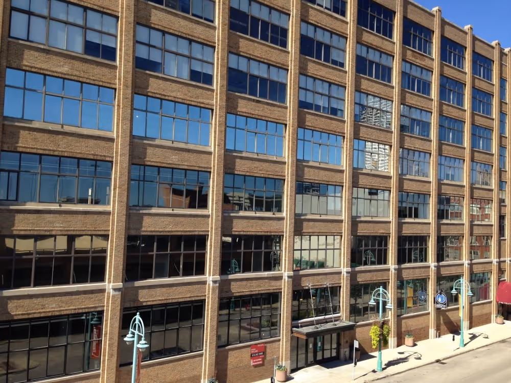 Brick office building with multiple windows reflecting blue sky and street lamps along sidewalk.