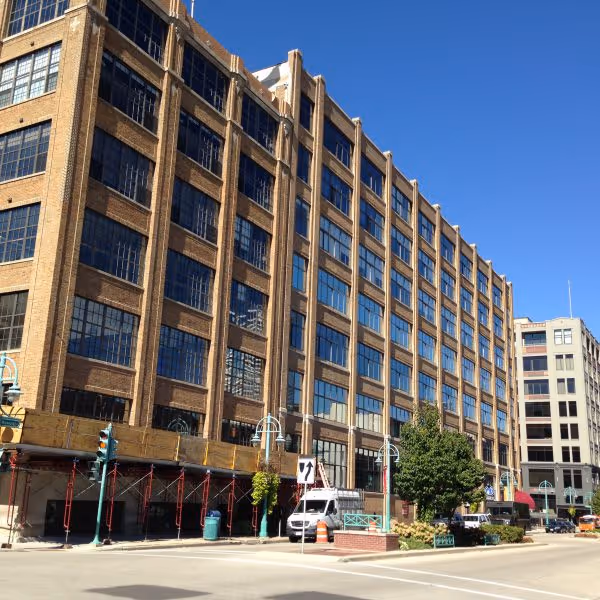 Multi-story brick office building with many windows under clear blue sky on city street corner.