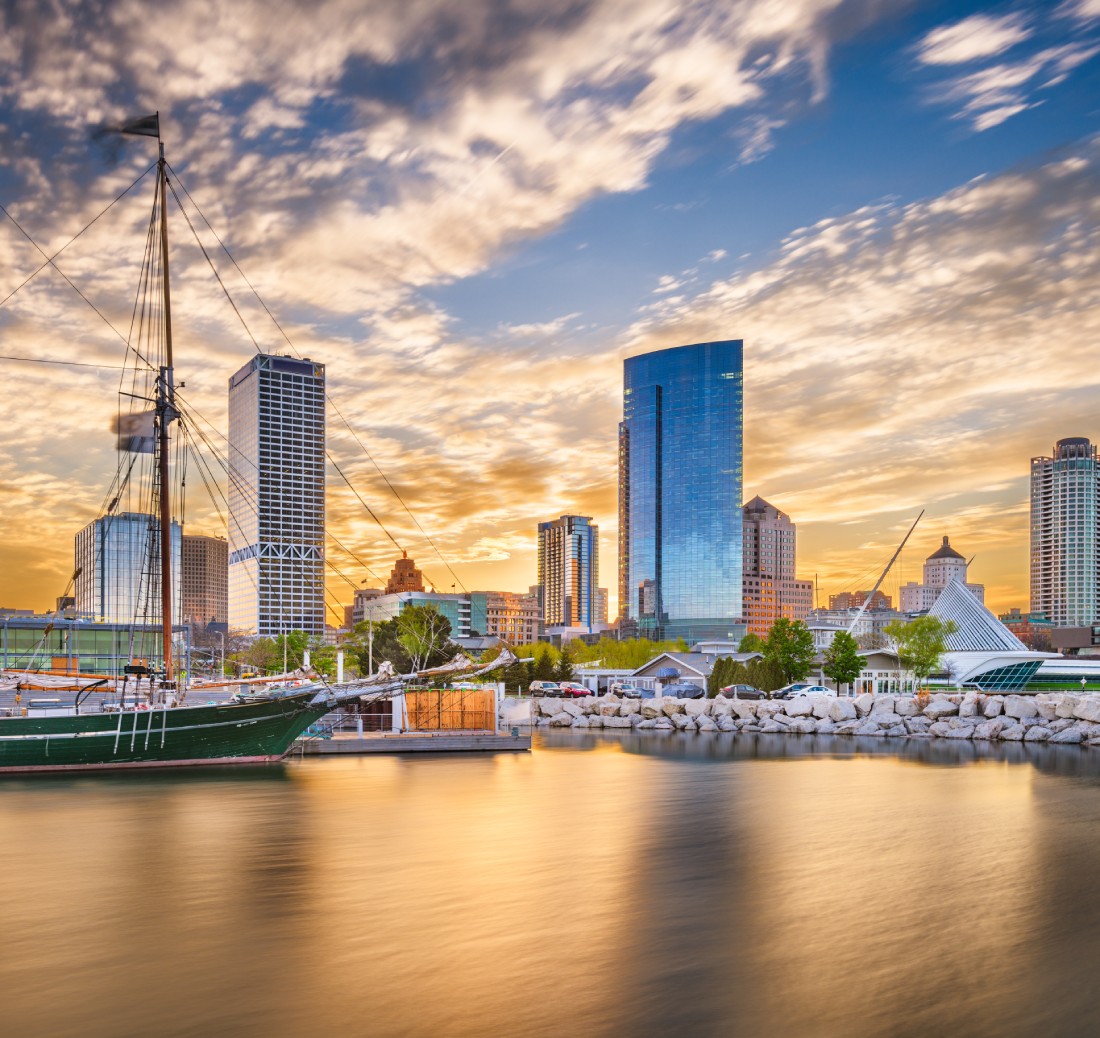 Milwaukee skyline at sunset with sailboat docked and golden reflections on water.
