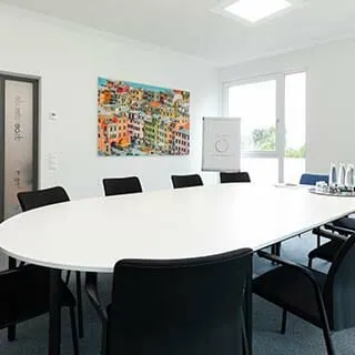 Moderner Besprechungsraum mit weißem Tisch, schwarzen Stühlen, Fenster und farbigem Wandbild.