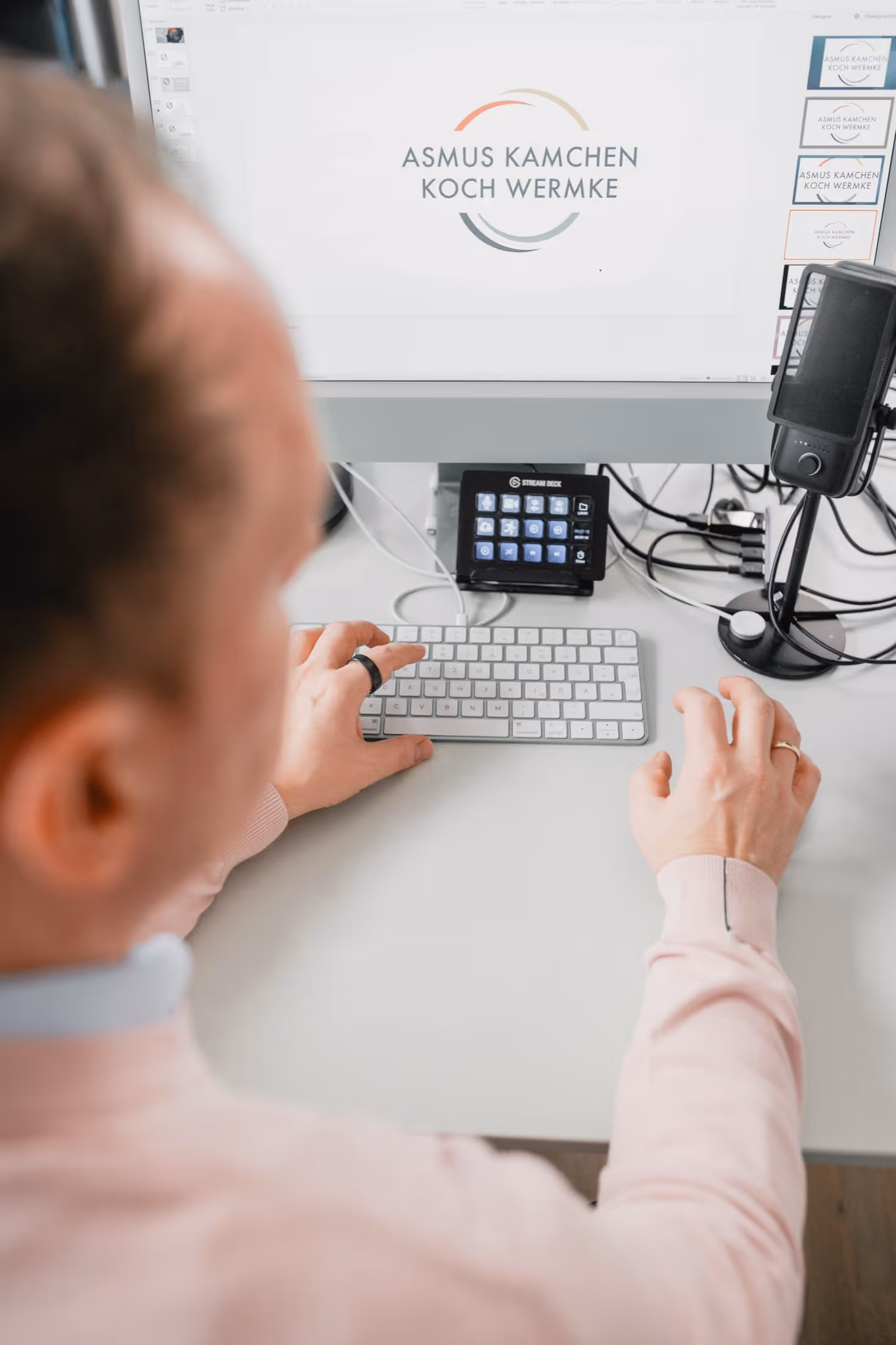 Person arbeitet an einem Computer mit Tastatur, Stream Deck und Mikrofon auf dem Schreibtisch.