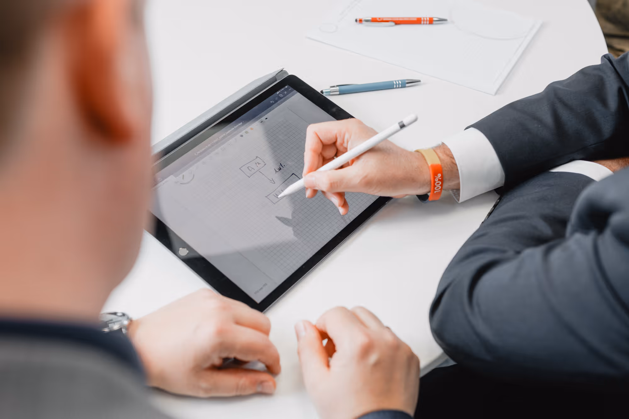 Zwei Männer arbeiten an einem Tablet, einer skizziert ein Diagramm mit einem Stift.