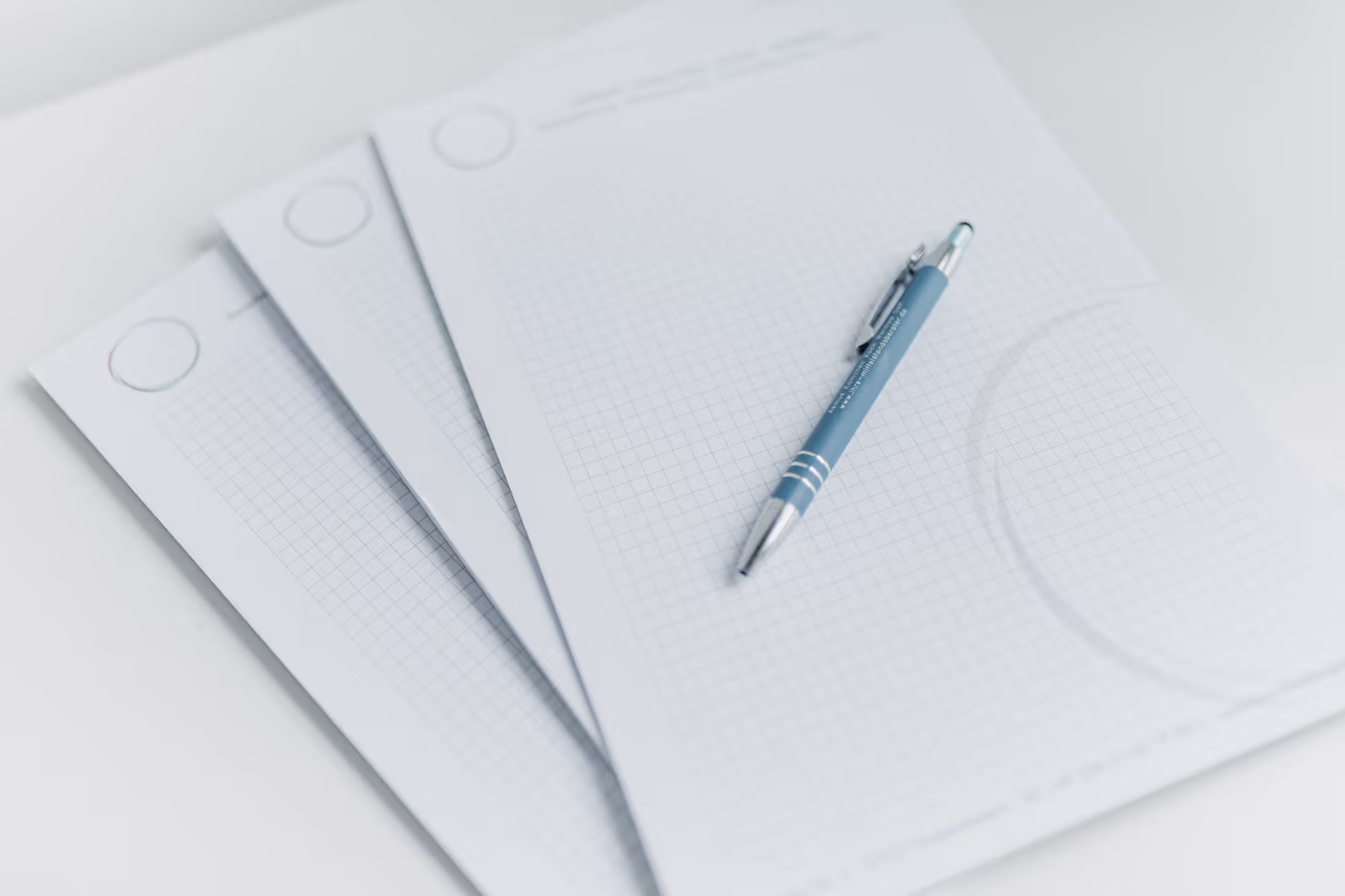 Drei kariert Blattpapiere, auf dem oberen liegt ein blauer Stift mit Clip.