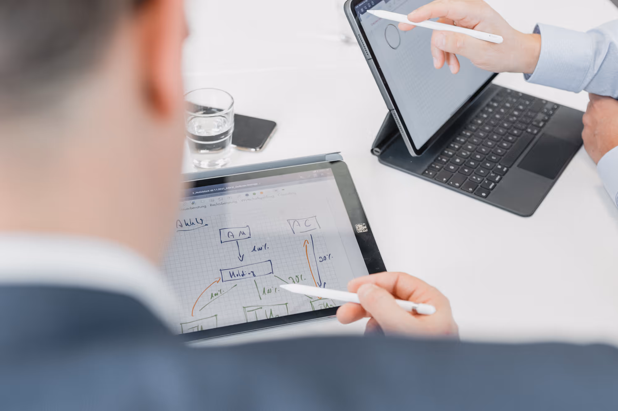 Zwei Personen markieren mit Stiften auf Tablets digitale Diagramme auf einem weißen Schreibtisch.