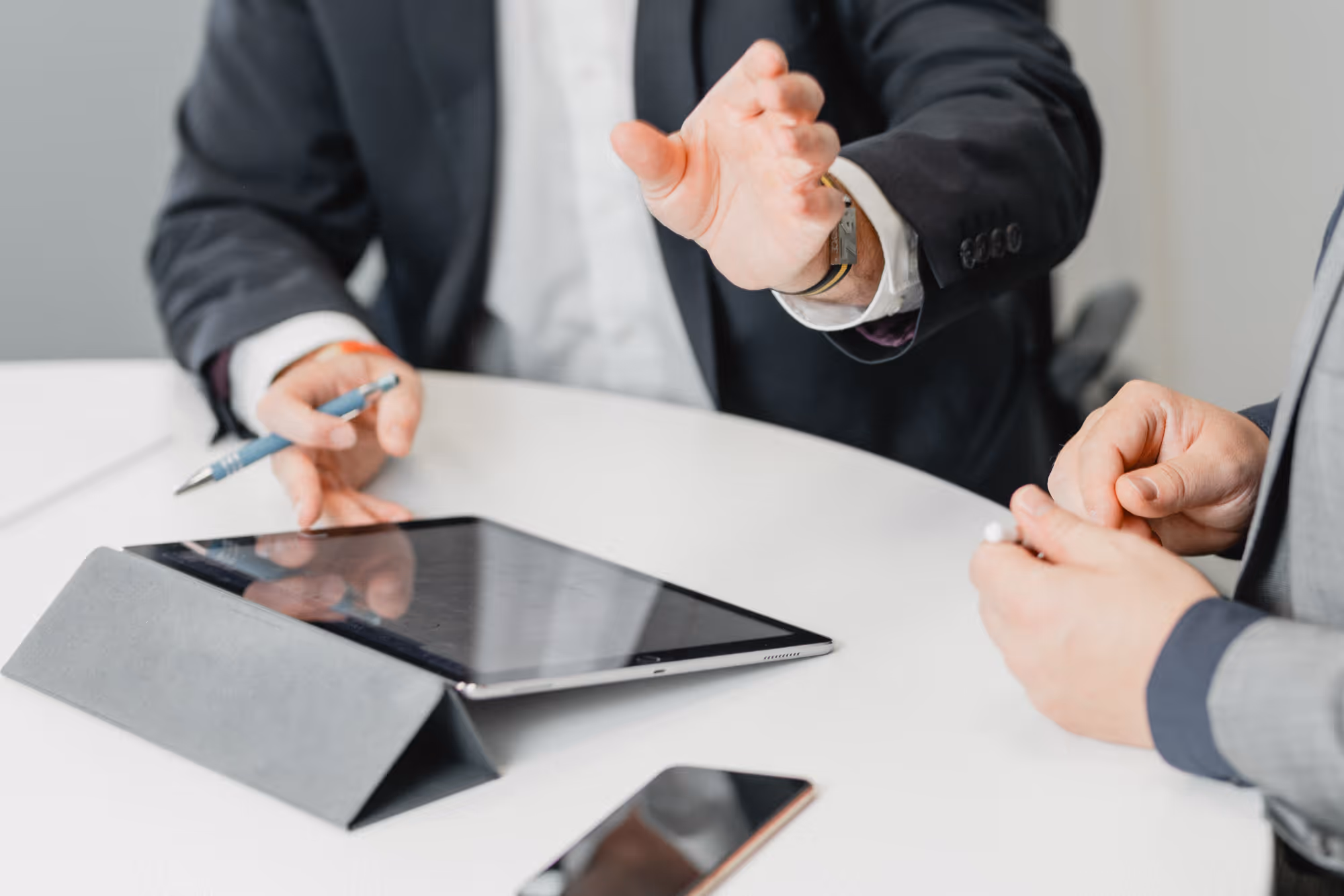 Zwei Geschäftsmänner diskutieren über ein Tablet auf einem weißen Tisch mit Smartphone.