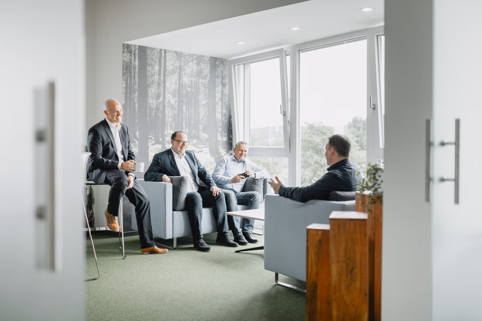Vier Männer in einem modernen Büro unterhalten sich entspannt auf Sesseln und einem Hocker.