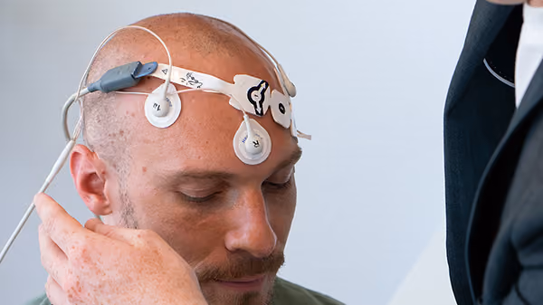 Mann mit Elektroden am Kopf, die wahrscheinlich für neurologische Messungen angebracht sind.