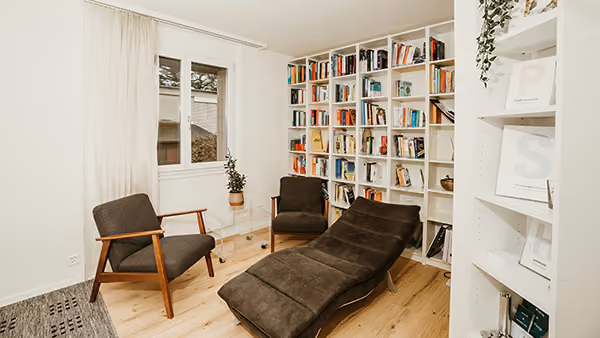 Gemütlicher Raum mit zwei Stühlen, Chaise Lounge und einem Bücherregal voller Bücher.