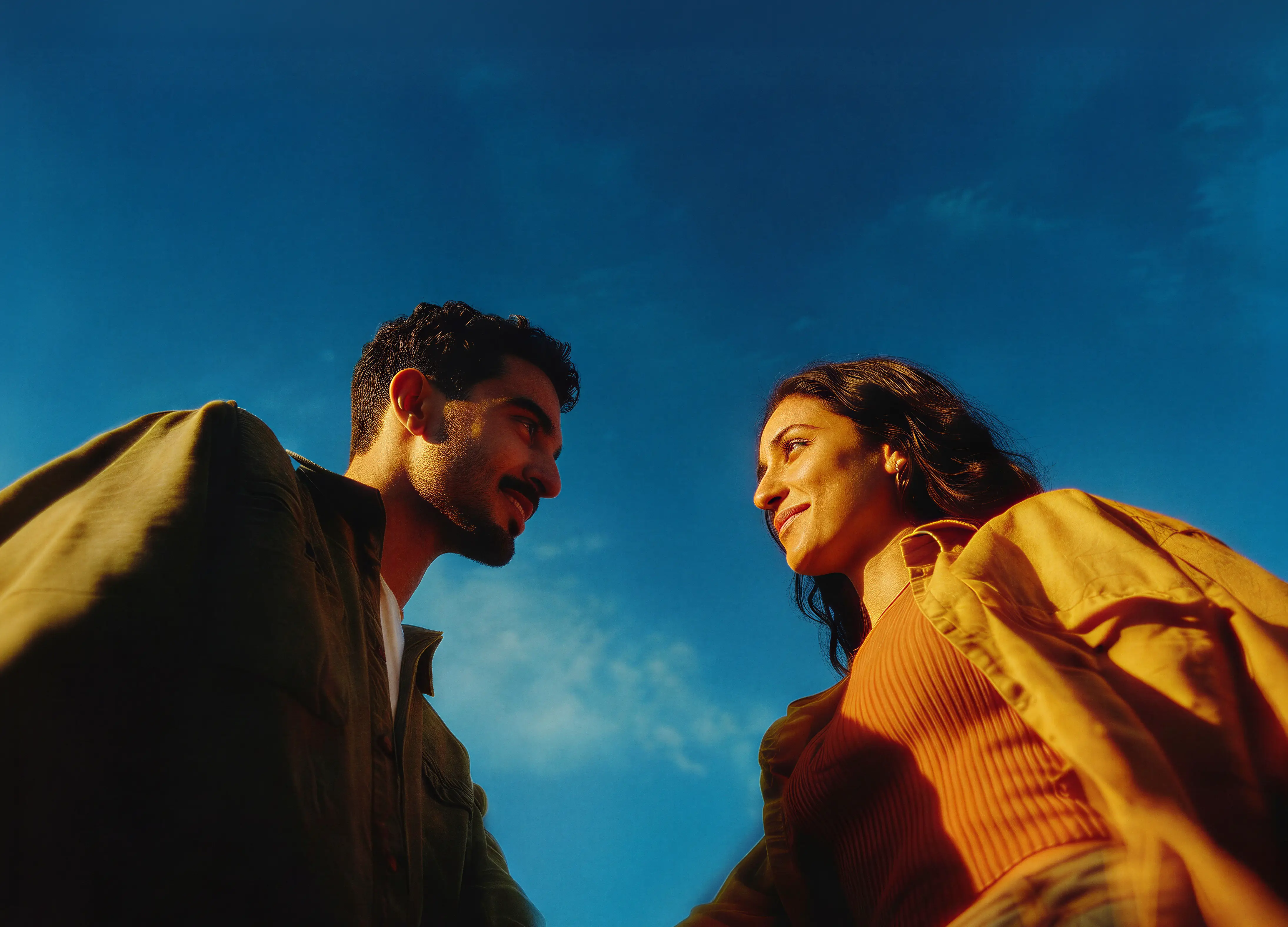 Man and woman smiling at each other against a clear blue sky background.
