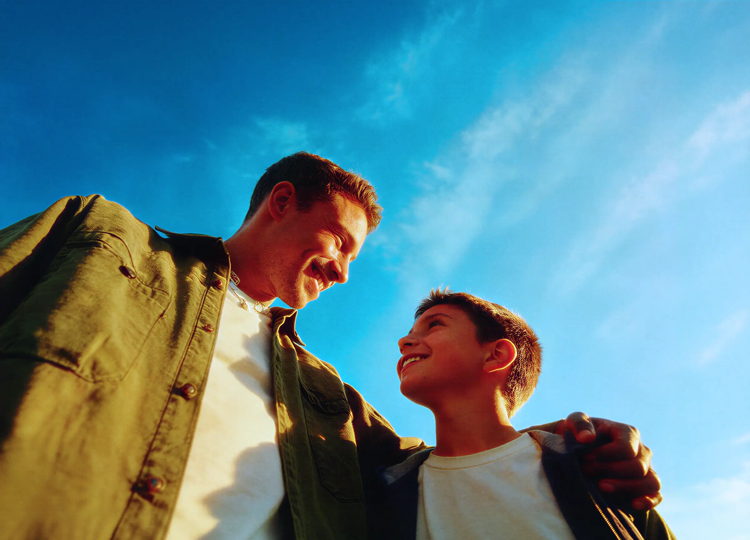 Smiling man and boy looking at each other against a clear blue sky.