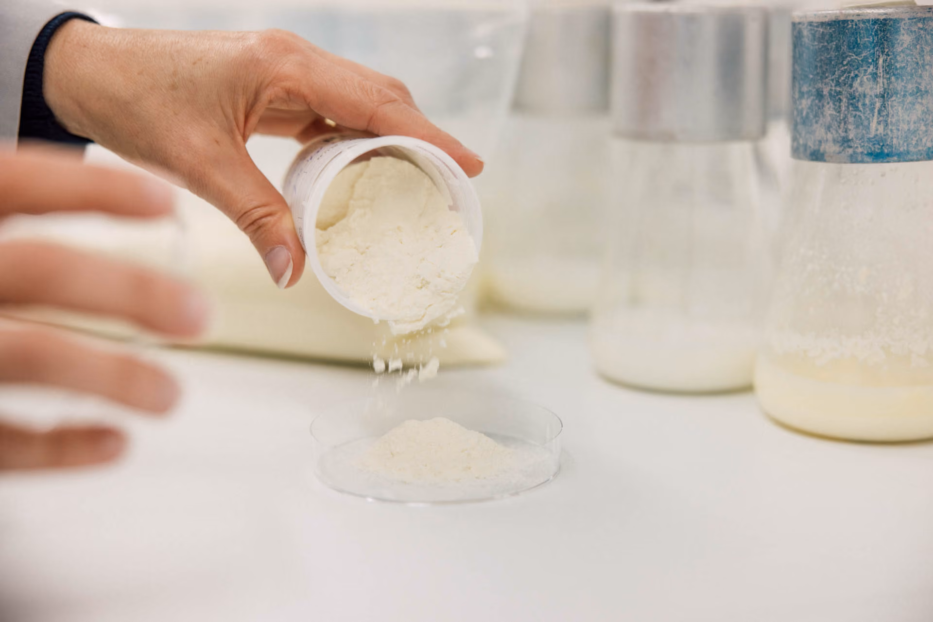 Una mano versa polvere bianca da un contenitore in una capsula petri in un laboratorio.
