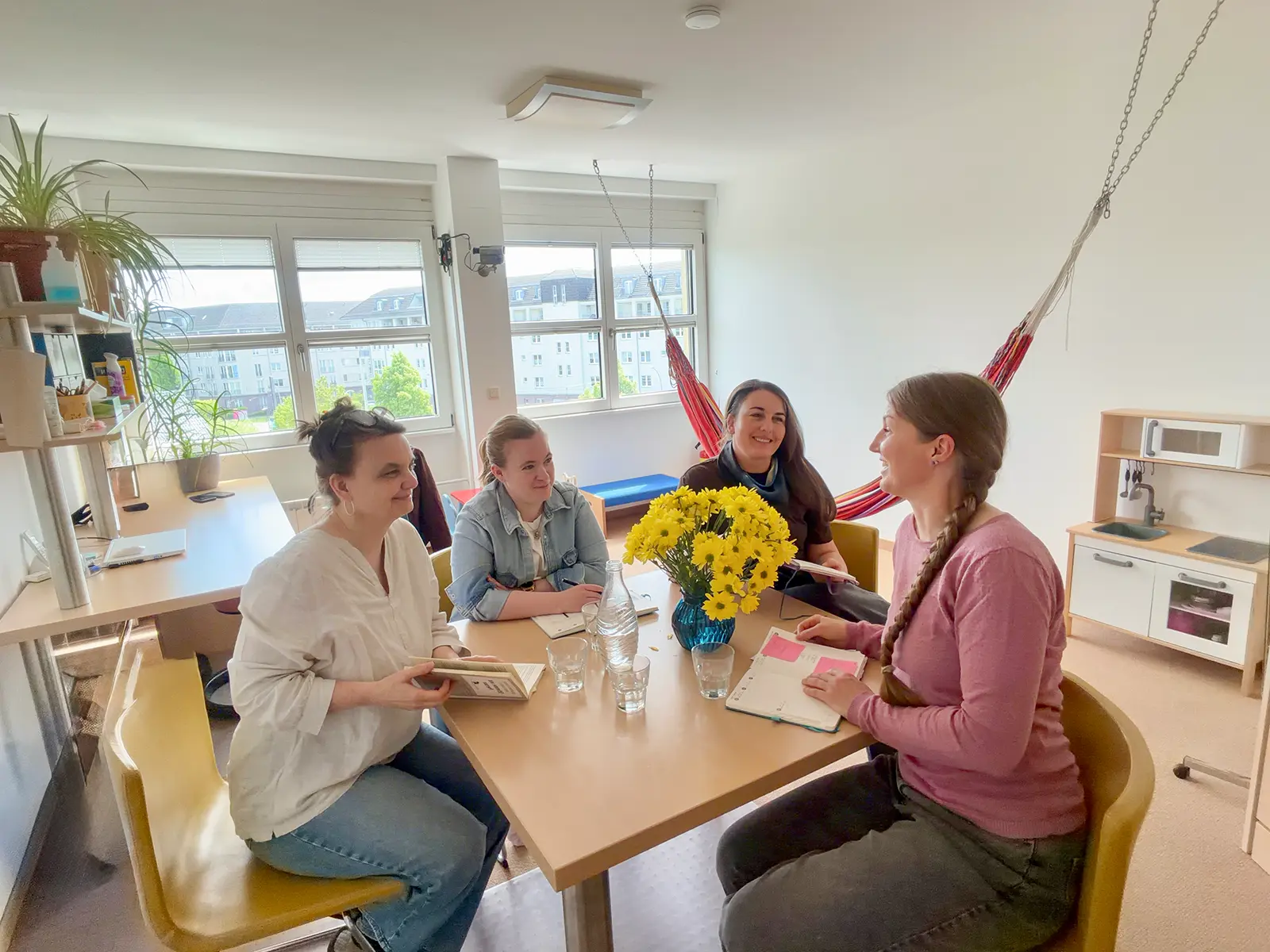 Elisabeth Warnke und ihr Team sitzen an einem Tisch mit Blumen, Büchern und Glasflaschen in einem hellen Raum.