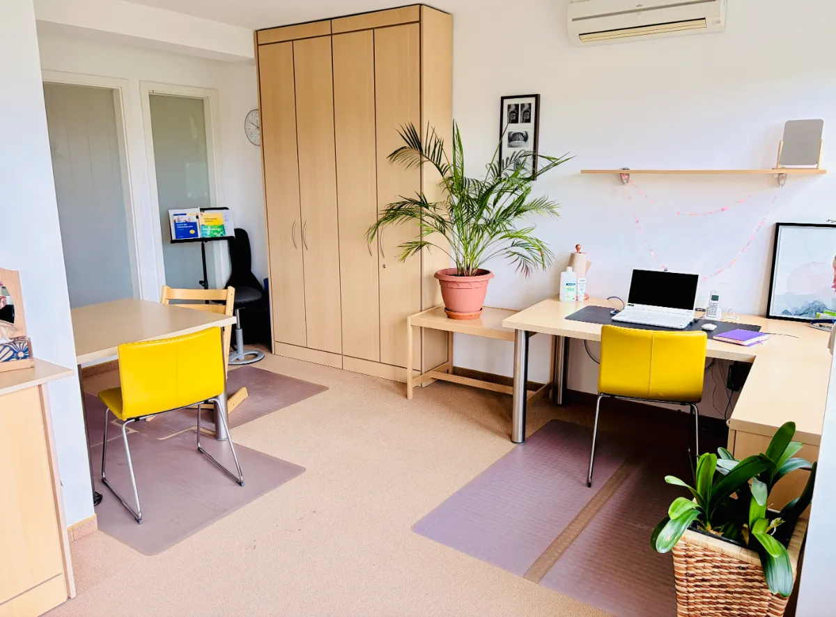 Helles Büro mit zwei gelben Stühlen, Schreibtischen, Pflanzen und einem Laptop.