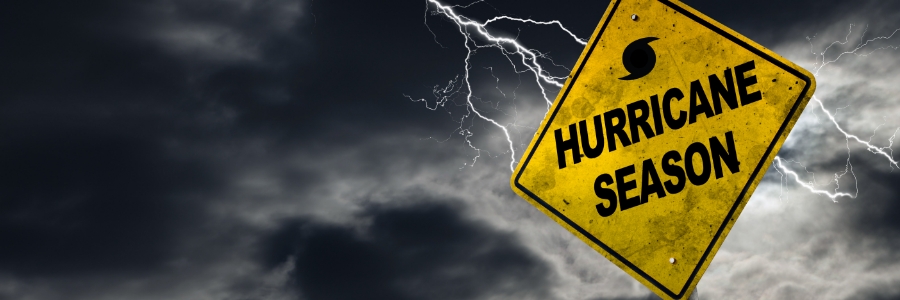 Yellow diamond warning sign reading Hurricane Season against stormy dark sky with lightning bolts