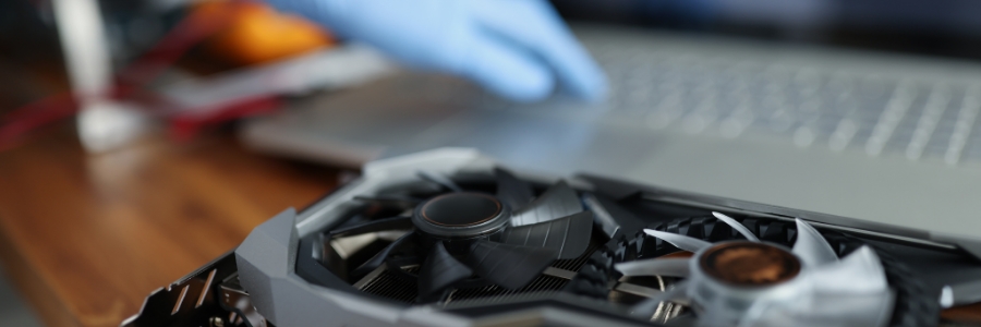 Technician in blue gloves handling a GPU graphics card near a laptop for PC hardware maintenance