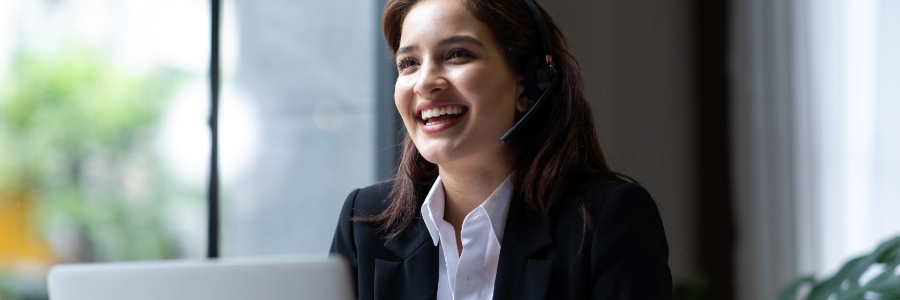 Smiling businesswoman wearing a call center headset while working on a laptop in a modern office