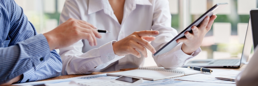 Two professionals reviewing IT data on a tablet and printed reports during a business technology consulting meeting