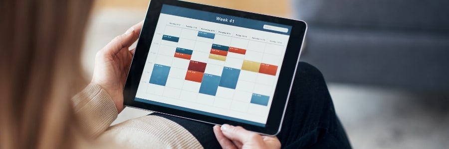 Person holding tablet displaying a weekly Microsoft 365 calendar schedule with color-coded appointments
