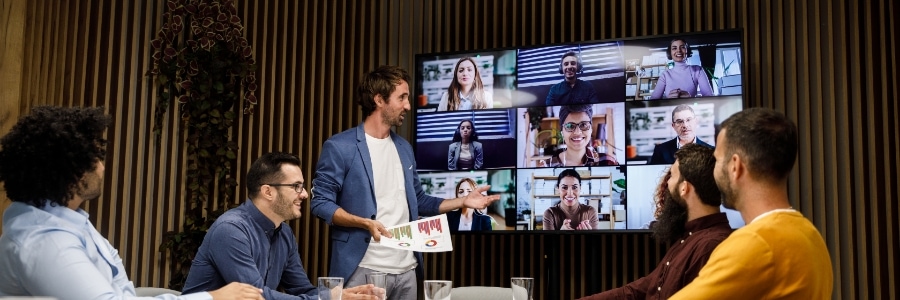 Hybrid team meeting with presenter sharing documents while remote colleagues join via video conferencing screen