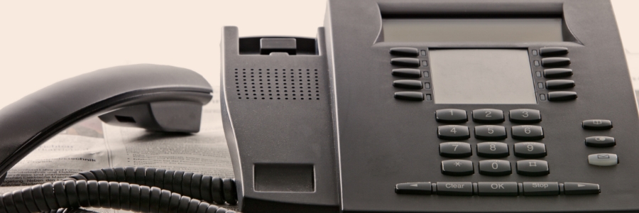 Black office VoIP desk phone with handset, keypad, and display screen on a business desk