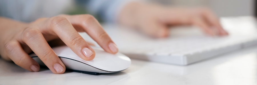 Person using a white wireless computer mouse and keyboard on a desk for IT productivity tasks