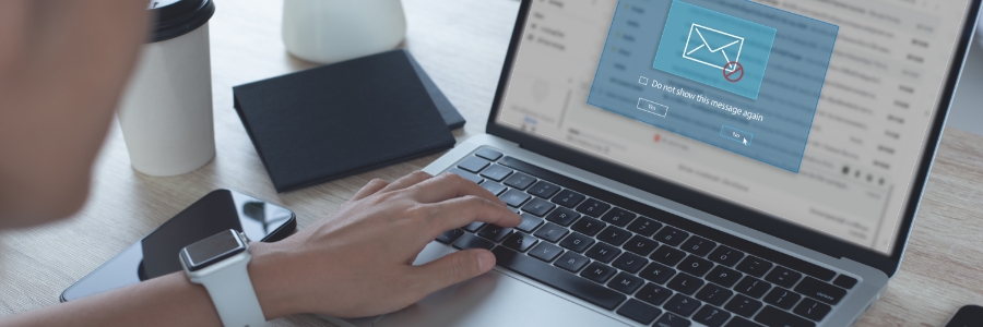 Person typing on laptop displaying email notification popup, with smartphone and smartwatch on desk nearby