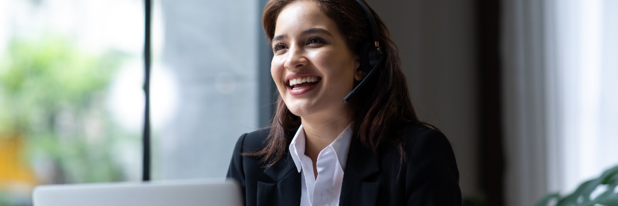 Smiling businesswoman using a VoIP headset while working on a laptop in a modern office