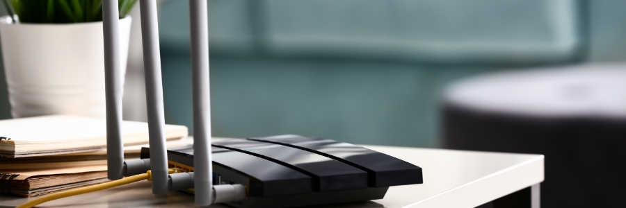 Black wireless router with three antennas on a desk, with ethernet cables connected, in a modern office setting