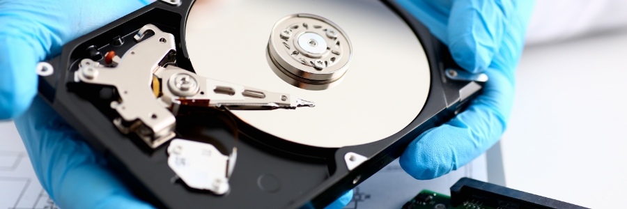Technician in blue gloves holding open hard disk drive showing internal platters and read-write arm components